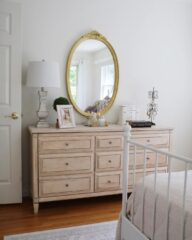 A wooden dresser in a bedroom with a gold mirror above it.