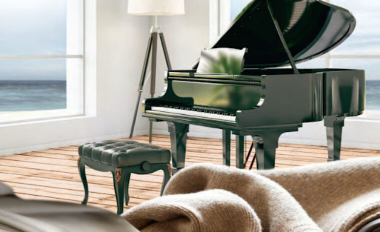 This living room has a sofa with a blanket laying across it and a green piano and piano bench placed in the middle of the room overlooking the view of the ocean.